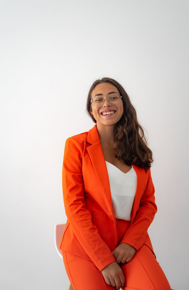 Clara im orangefarbenen Anzug mit Laptop